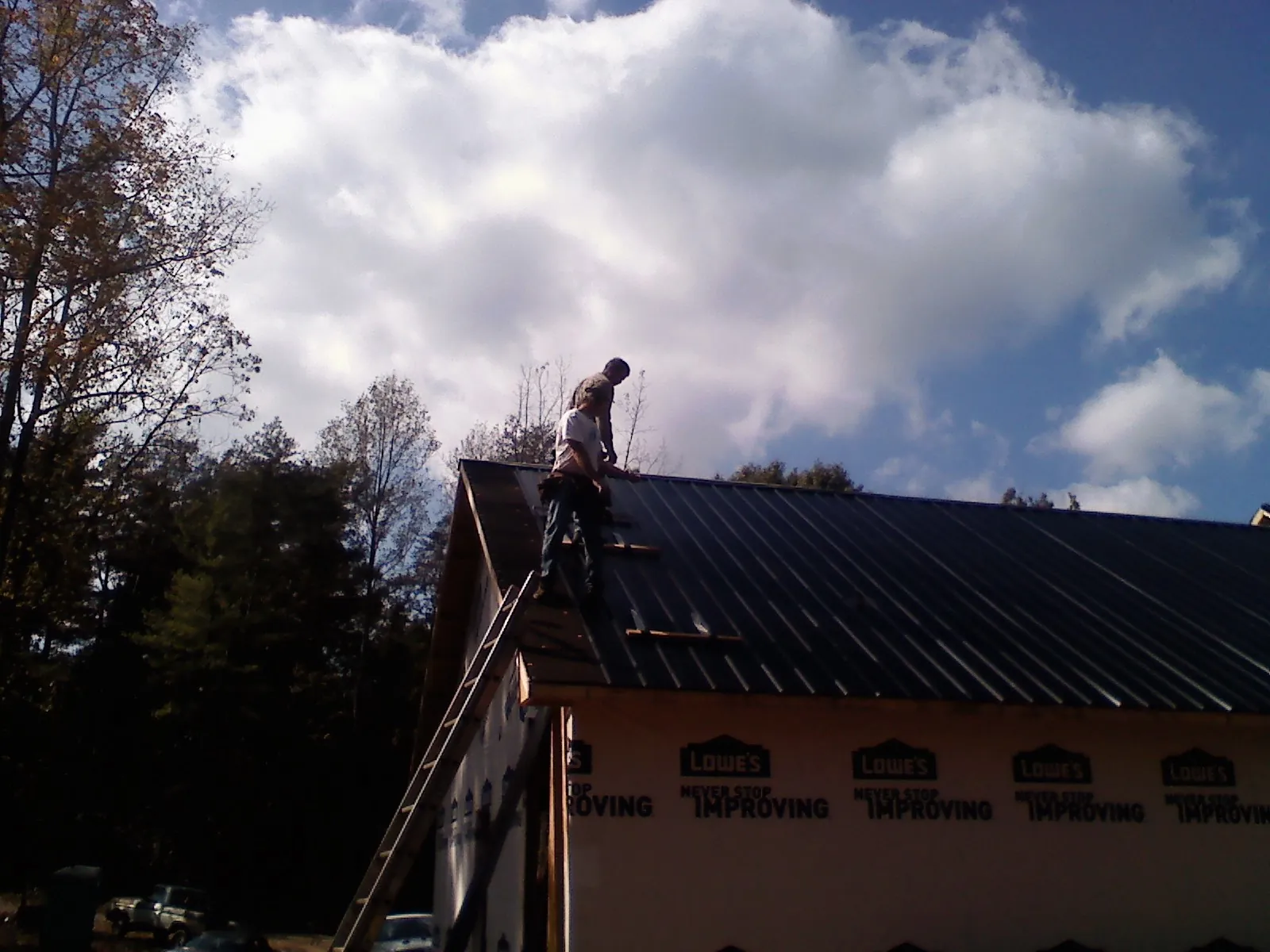 Roofer fastening dark metal panels high against a cloudy sky, from a Roof Inspection job in Westphalia