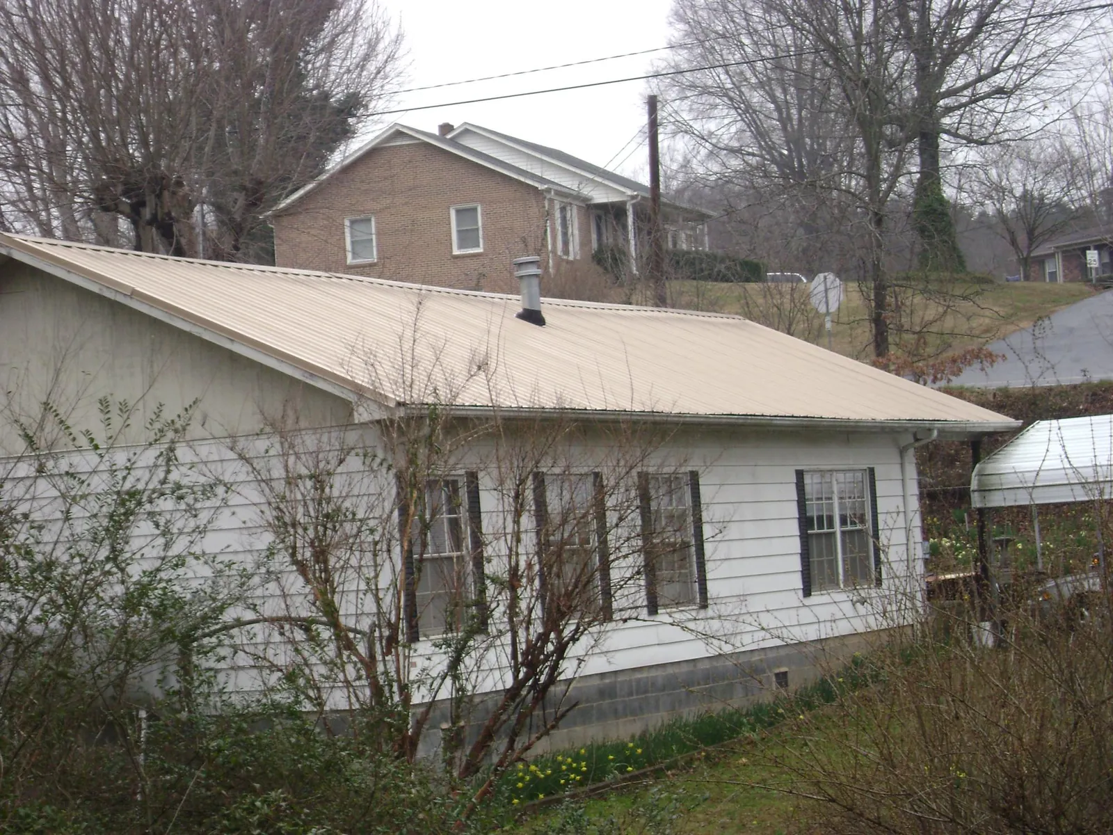 Tan metal roof on a white sided house set into a hillside — Commercial Roofing by Roofing Brothers in Westphalia